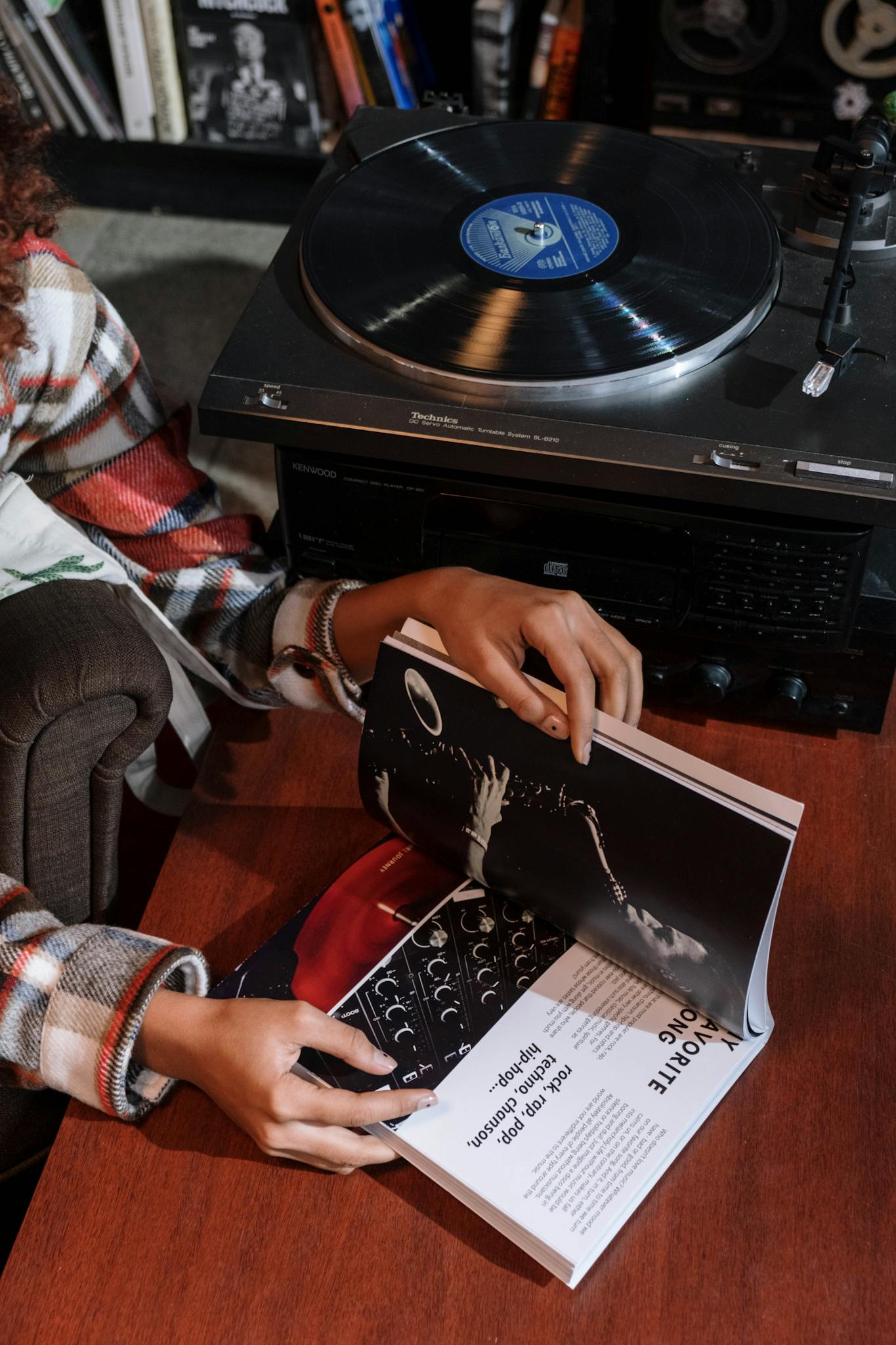 A person reads a music magazine near a vintage vinyl turntable indoors.